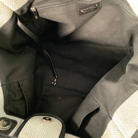 Interior of grey woven Chanel tote showing black fabric lining, zip pocket, leather-trimmed pockets, branded interior plaque, and magnetic snap closure.