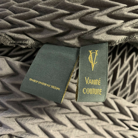 Close-up of VANITE COUTURE garment labels on chevron-pleated fabric.