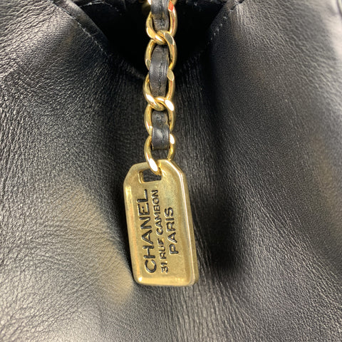 Close-up of gold-tone Chanel Paris hangtag attached to leather-woven chain.