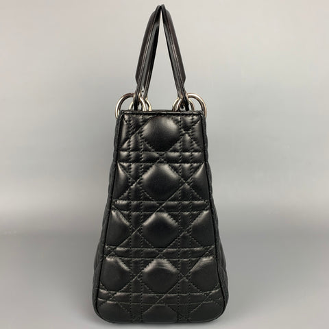 Side view of the structured black quilted handbag showing its gusseted profile and top handles.