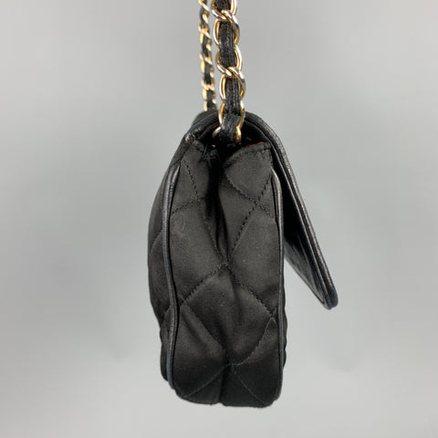 Opposite side view of black quilted handbag with flap slightly raised.