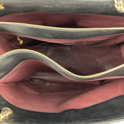 Interior view of black handbag with burgundy lining, gold-tone zipper teeth, divided compartments, and a burgundy zip pocket.