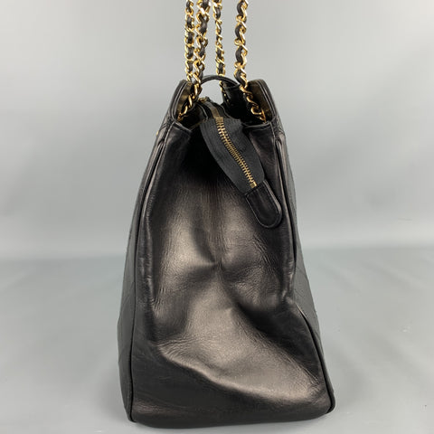 Side view of black leather handbag showing the gold-tone zipper and structured side panel.