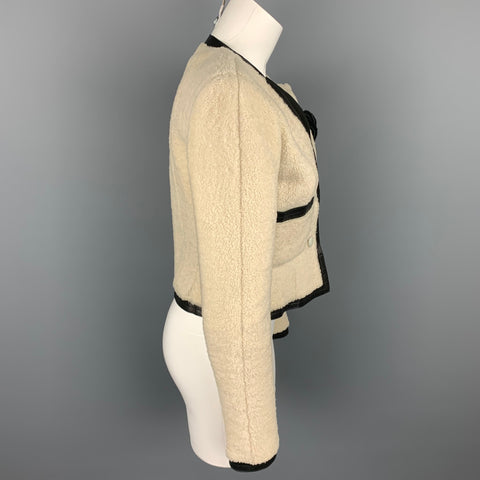 Side view of the cream shearling jacket showing long sleeve, fitted waist, and black-trimmed hem.