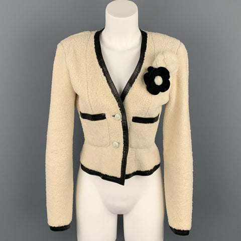Front view of cream shearling Chanel jacket on mannequin with black leather trim, black camellia applique, front pockets, and two buttons.