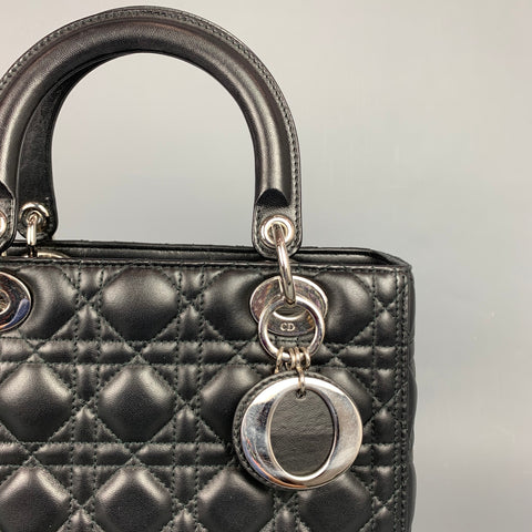 Close front detail of the black quilted handbag, top handle attachment, silver-tone hardware, and Dior letter charm.