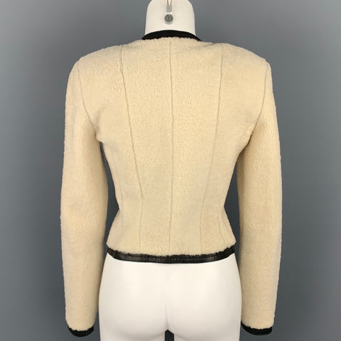 Back view of cream shearling jacket with long sleeves, fitted shaping seams, and black leather trim at hem.
