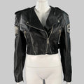 A black leather biker jacket with silver tone patches and zip pockets, displayed on a mannequin.