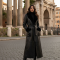 A black shiny lamb shearling coat with a large lapel, flap pockets, and fur trim, featuring a hook & eye closure.