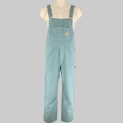 CARHARTT brand light blue cotton overalls displayed on a mannequin, featuring adjustable elastic suspenders, a bib pocket, back pockets, and a zip fly closure.